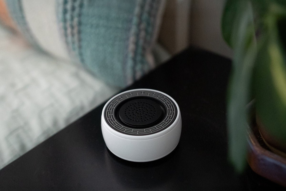White SIBŌ sound bath device on a black bedside table beside a pillow