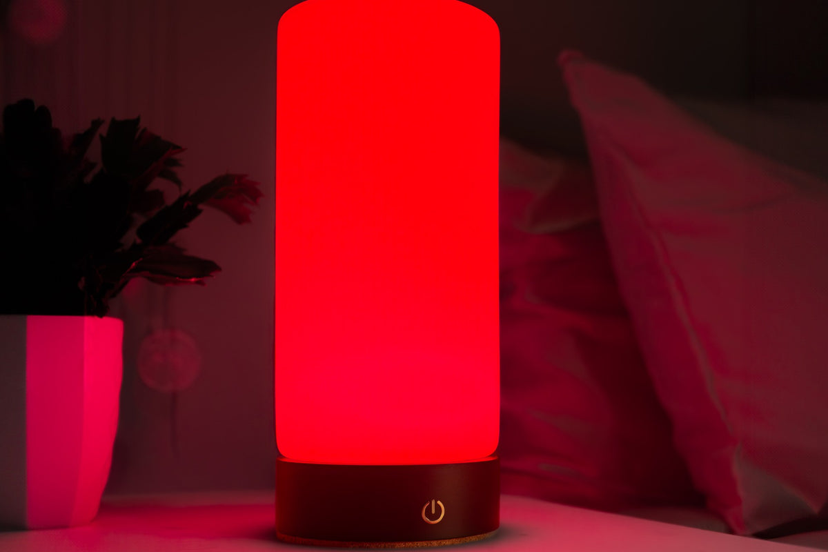 RŪBI glowing red on a white bedside table beside pillows and a potted plant