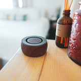 TŌNEM sound therapy speaker with wood housing on a sunlit wooden table beside a reed diffuser