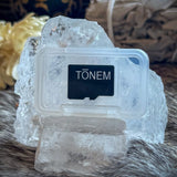 Close-up of the TŌNEM Tone Card micro SD card with printed TŌNEM logo, resting on a quartz crystal in front of a singing bowl